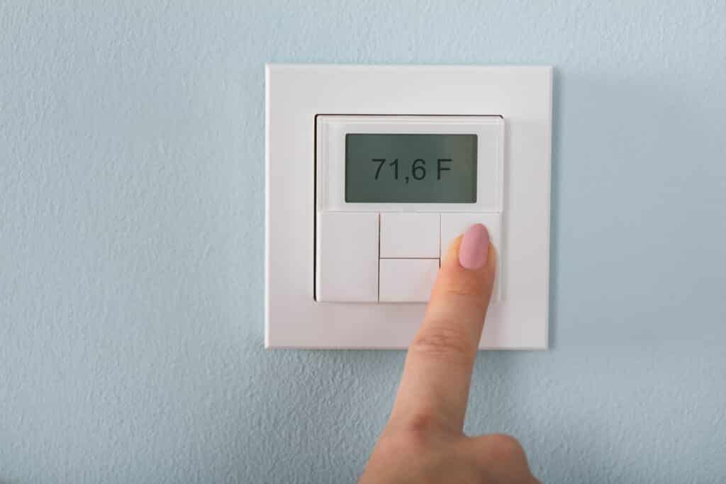 A hand sets the temperature in a thermostat.