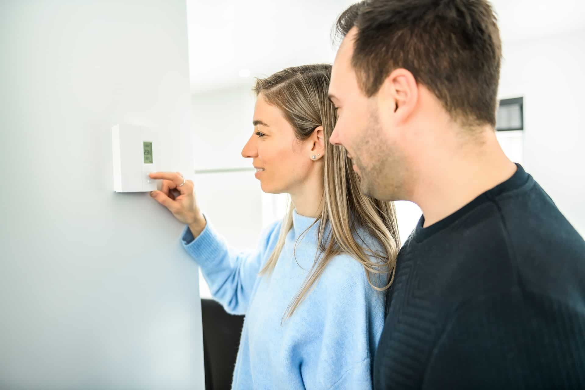 A couple sets the thermostat in their home.